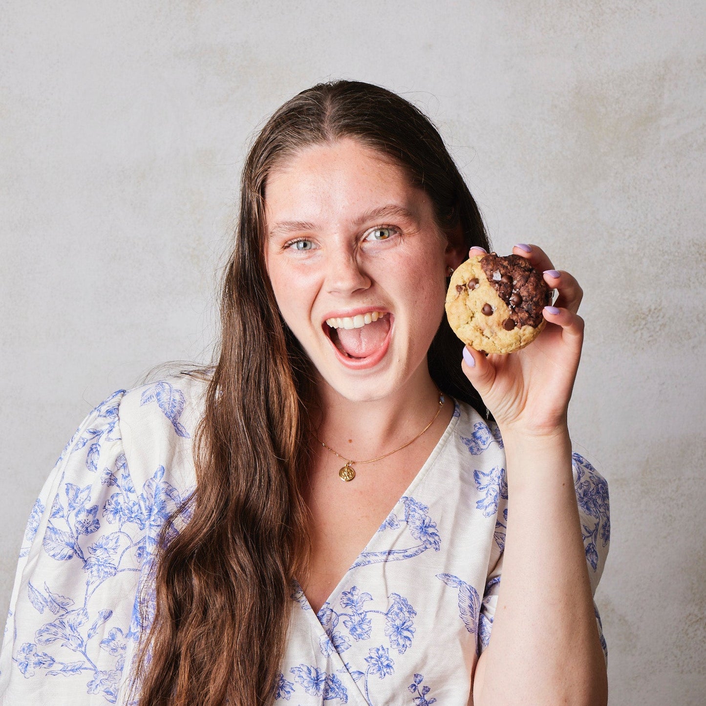 Freya Cox in a floral dress holding a cookie against a plain background
