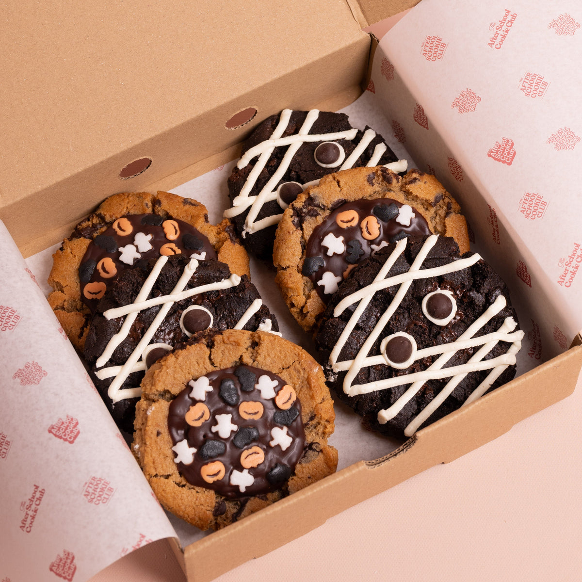 Three double chocolate cookies decorated as mummies, three chocolate chip cookies decorated with halloween sprinkles in a box