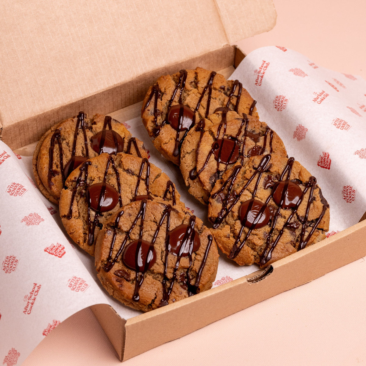 Box of cookies with chocolate drizzle on a pink background