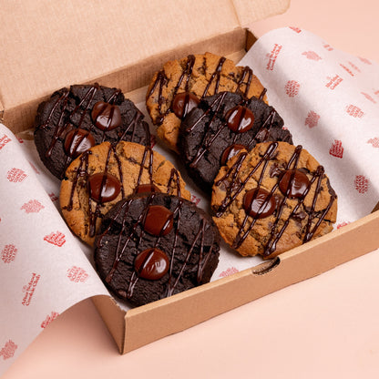 Box of chocolate chip and double chocolate cookies with chocolate drizzle on a pink background