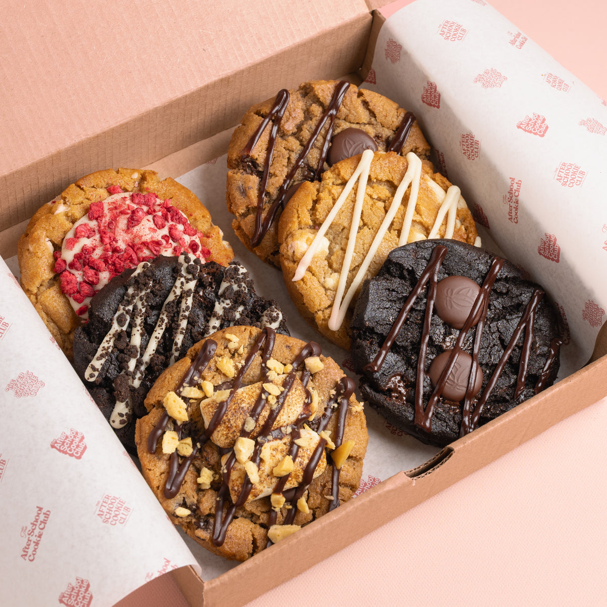 A box of six assorted gourmet chocolate cookies arranged inside a brown cardboard box lined with branded white paper. 