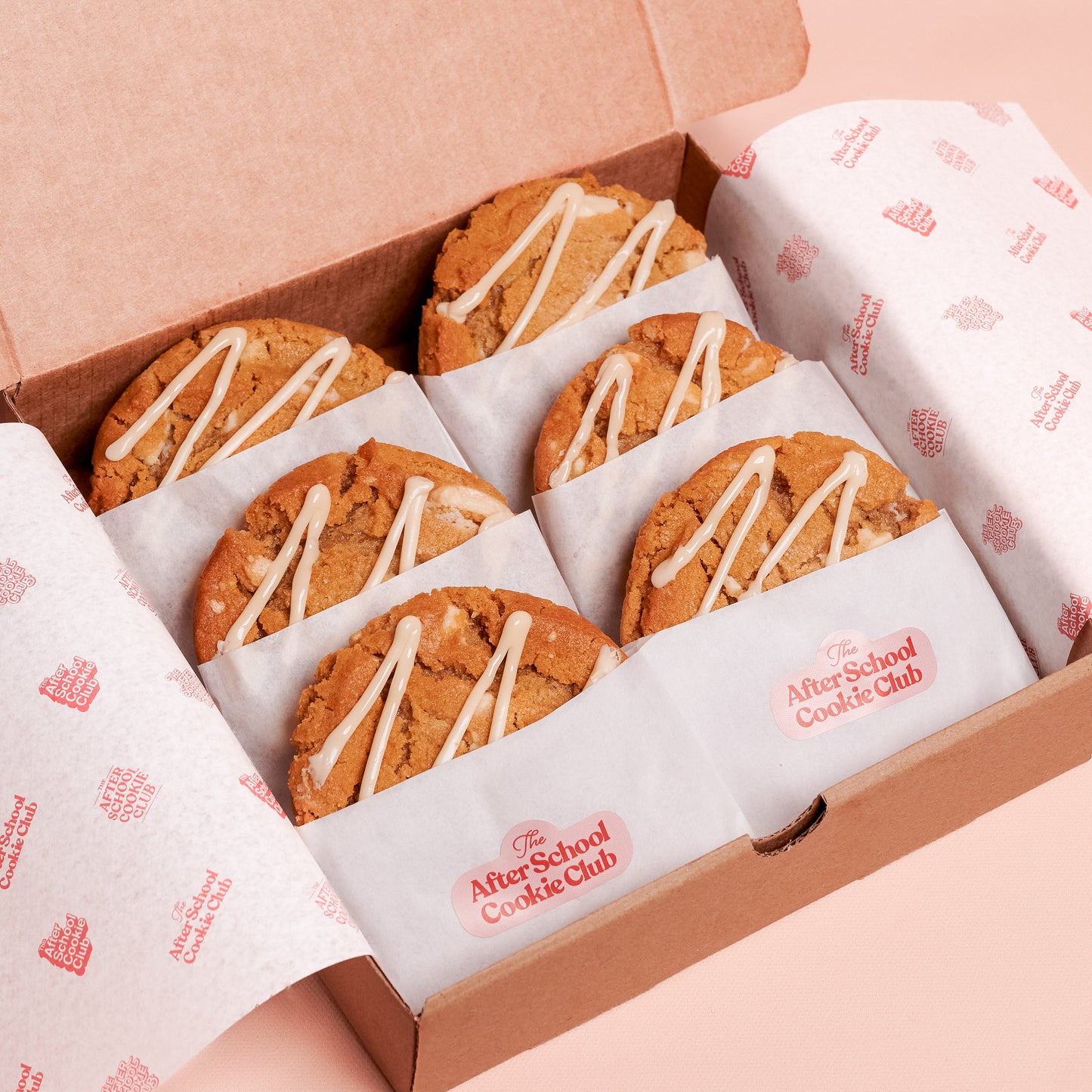 Box of white chocolate cookies with white drizzle on a pink background