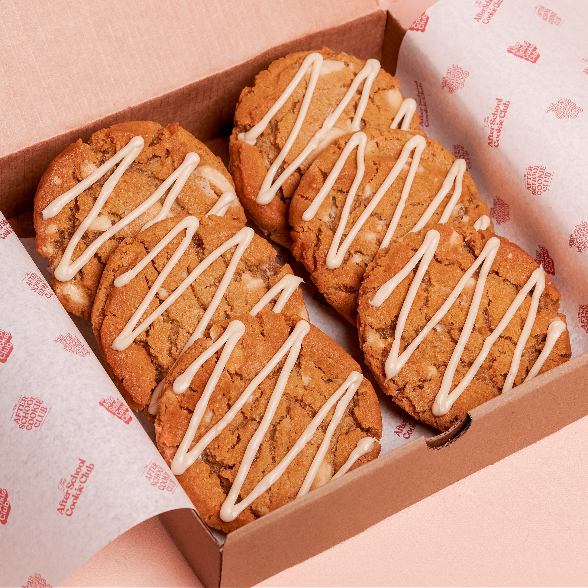 Box of white chocolate cookies with white drizzle on a pink background