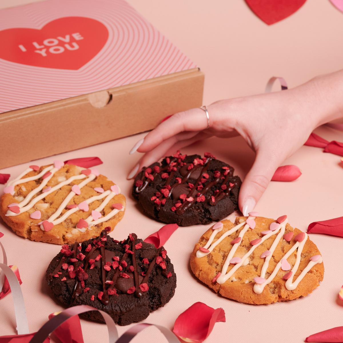 Box of four cookies decorated with heart sprinkles for valentine's day and hand grabbing one cookie