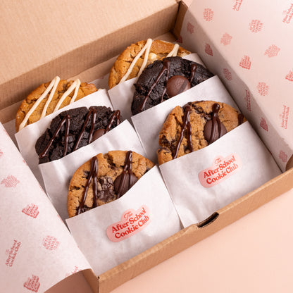 A box of six cookies from the After School Cookie Club, individually wrapped in branded white paper and arranged inside a brown cardboard box.
