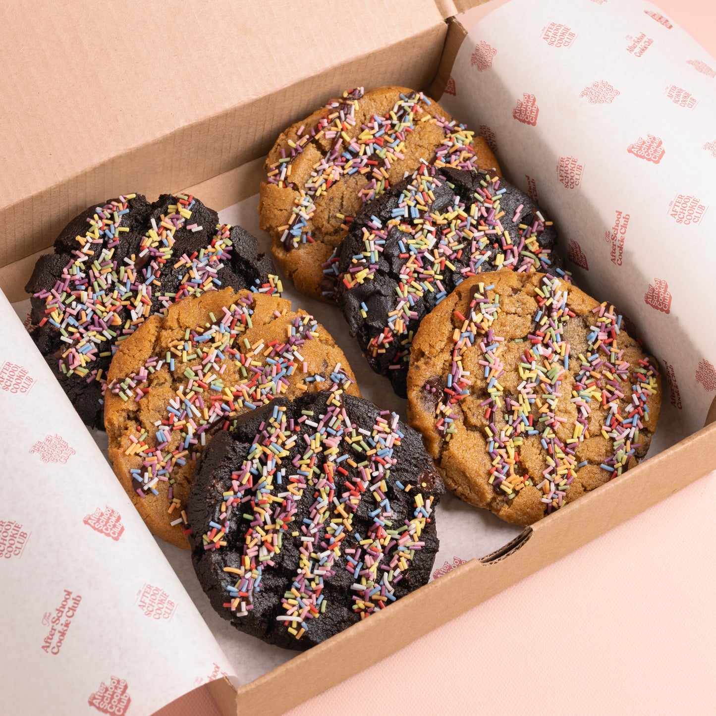 The cookies are arranged in two rows of three, with three double chocolate chip cookies and three choc chip cookie, each topped with colourful rainbow sprinkles.