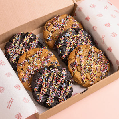 The cookies are arranged in two rows of three, with three double chocolate chip cookies and three choc chip cookie, each topped with colourful rainbow sprinkles.